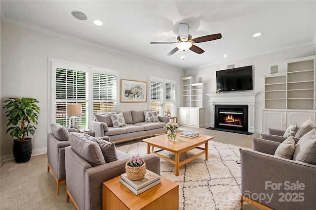 living area with a fireplace with flush hearth, baseboards, light colored carpet, a ceiling fan, and crown molding