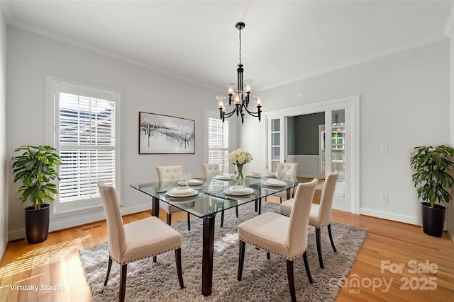 dining area with light wood-style flooring, ornamental molding, baseboards, and a notable chandelier