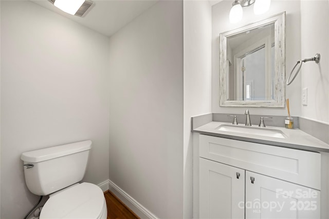 half bathroom featuring toilet, vanity, wood finished floors, and baseboards