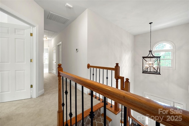 hallway featuring attic access, visible vents, a chandelier, an upstairs landing, and light colored carpet
