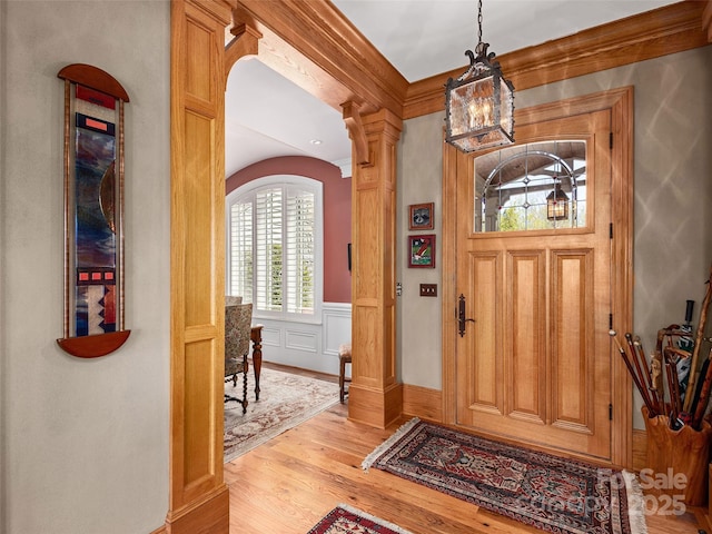 foyer entrance featuring an inviting chandelier, a wainscoted wall, light wood-style floors, ornate columns, and arched walkways
