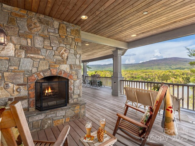 wooden deck with a view of trees, a mountain view, and an outdoor stone fireplace