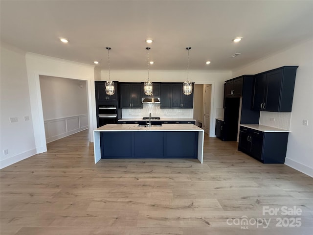 kitchen featuring decorative backsplash, ornamental molding, an island with sink, and light countertops