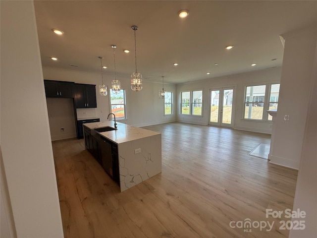 kitchen featuring a sink, baseboards, dark cabinetry, and light wood-style flooring
