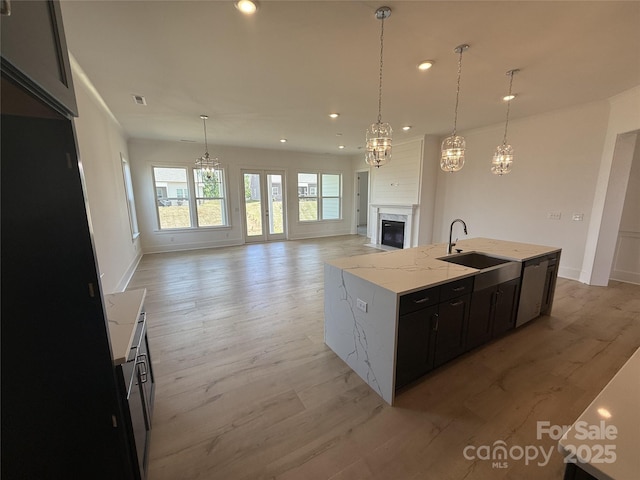 kitchen with recessed lighting, dark cabinets, a sink, a notable chandelier, and a premium fireplace
