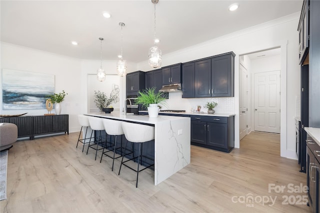 13279 Arnold Palmer Cir Unit 867, Lancaster, SC 29720 - kitchen with under cabinet range hood, gas stovetop, decorative backsplash, a breakfast bar area, and light wood finished floors