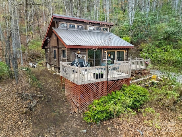 rear view of property featuring a deck, a wooded view, and metal roof