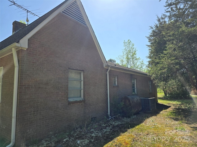 view of side of home with central AC unit, brick siding, heating fuel, and a chimney