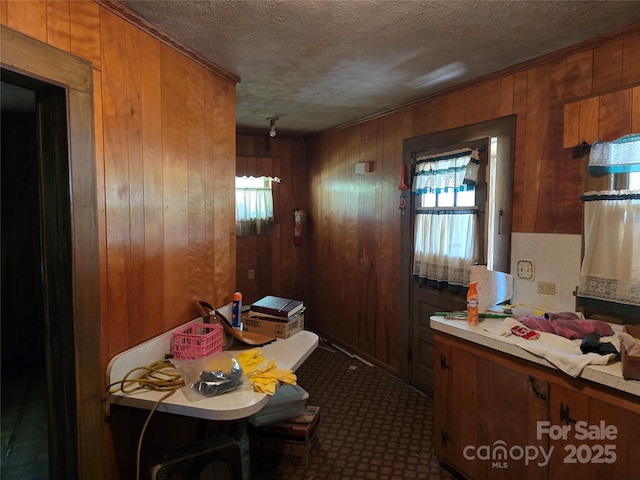 kitchen featuring dark carpet, light countertops, a textured ceiling, brown cabinets, and wood walls