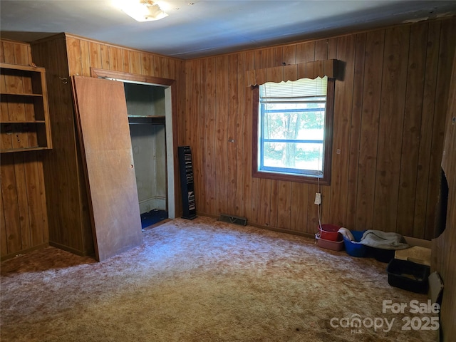 unfurnished bedroom featuring a closet, carpet flooring, wooden walls, and visible vents