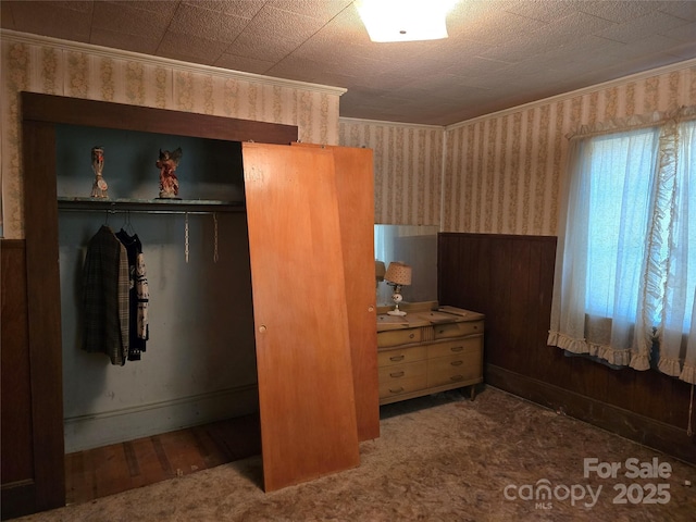 bedroom with a closet, wallpapered walls, ornamental molding, wood walls, and wainscoting