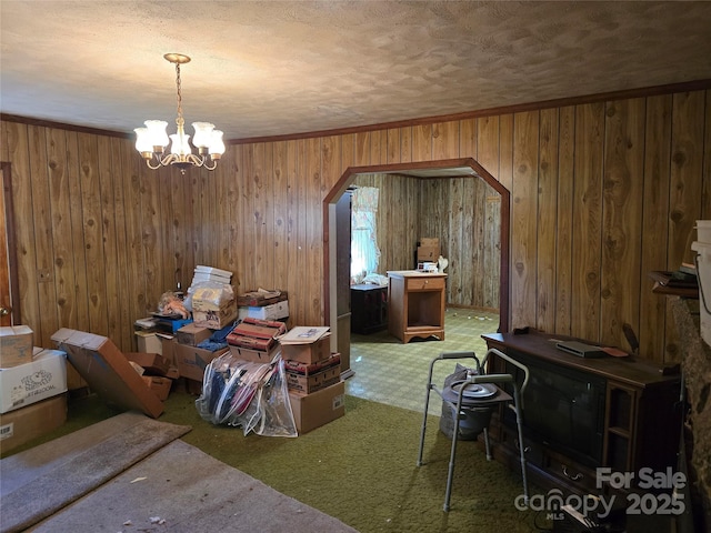 dining space with arched walkways, a notable chandelier, carpet, a textured ceiling, and wood walls