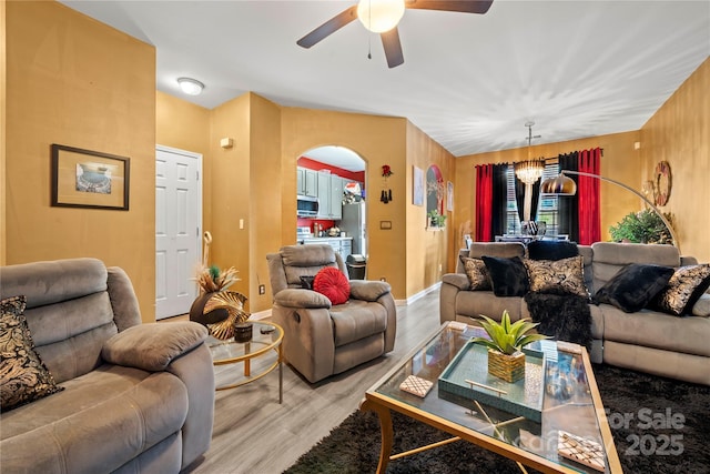 living area featuring baseboards, arched walkways, ceiling fan with notable chandelier, and light wood-style flooring