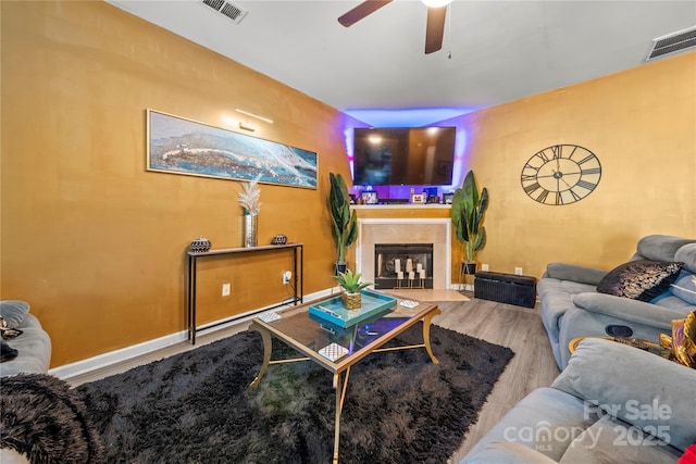 living area featuring wood finished floors, visible vents, a tiled fireplace, and a ceiling fan