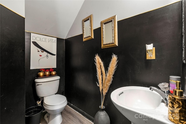 bathroom featuring wood finished floors, toilet, lofted ceiling, and a sink