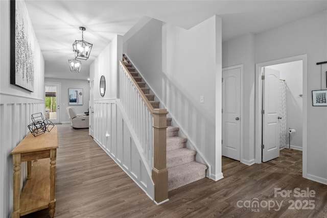 staircase with a chandelier, wood finished floors, and baseboards