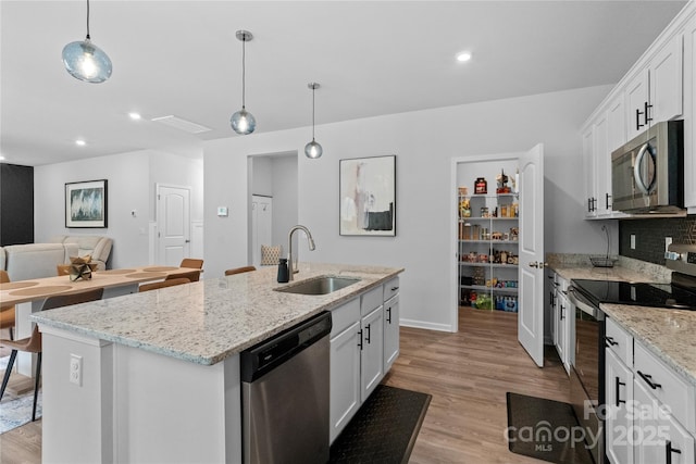 kitchen featuring an island with sink, light wood-style flooring, stainless steel appliances, and a sink