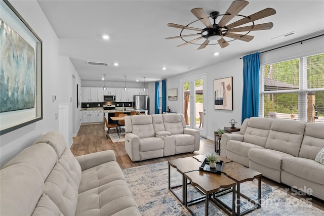 living room featuring light wood-type flooring, a ceiling fan, visible vents, and recessed lighting
