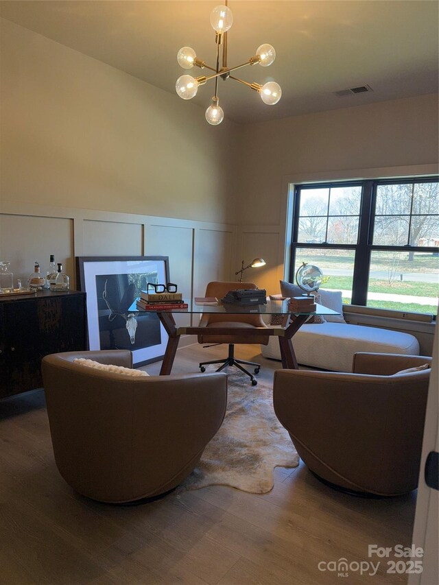 living room featuring a chandelier, a decorative wall, wood finished floors, and visible vents