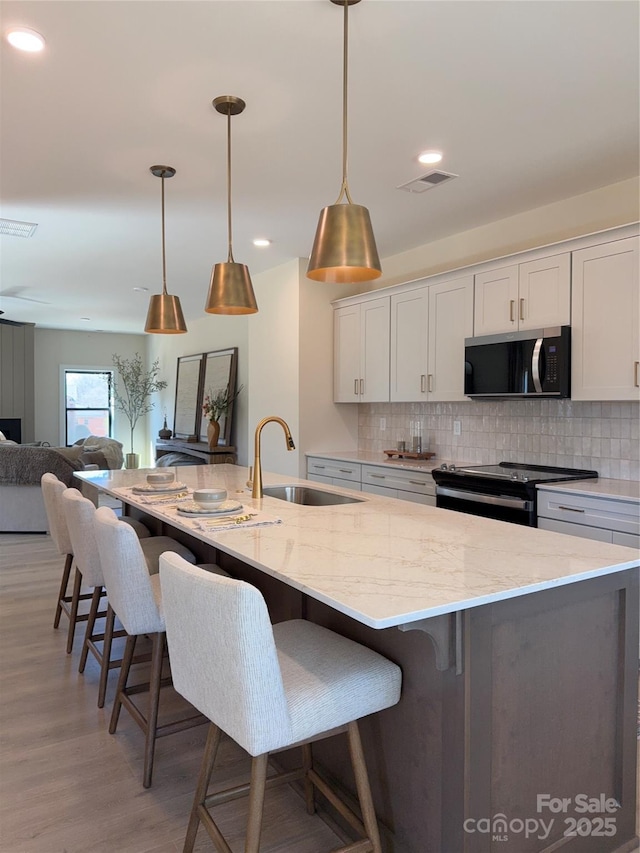 kitchen featuring visible vents, electric range oven, a sink, stainless steel microwave, and light wood finished floors