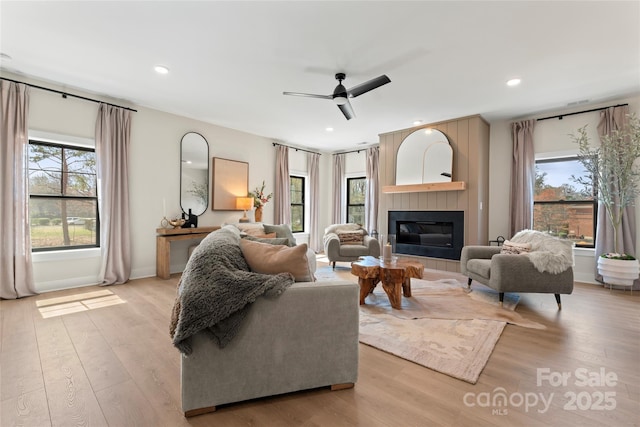 living area with light wood-style floors, a wealth of natural light, a ceiling fan, and a glass covered fireplace