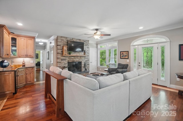 living room featuring baseboards, ceiling fan, a fireplace, dark wood-type flooring, and ornamental molding