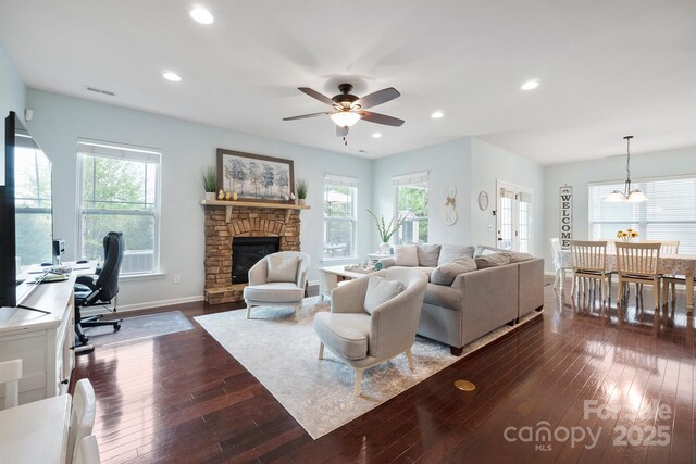 13115 Union Square Dr, Huntersville, NC 28078 - living room featuring baseboards, dark wood-style flooring, a stone fireplace, visible vents, and ceiling fan with notable chandelier