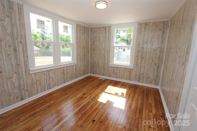 empty room with wooden walls, baseboards, hardwood / wood-style flooring, and visible vents