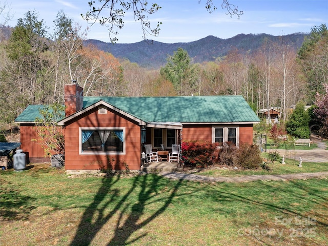 single story home with a chimney, a front lawn, a view of trees, a mountain view, and metal roof