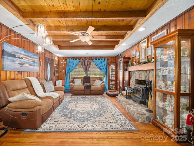living area featuring beam ceiling, a ceiling fan, wood finished floors, wood walls, and wooden ceiling