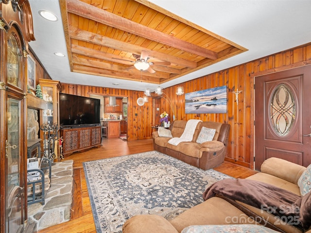 living room with wood walls, light wood-style flooring, and a tray ceiling