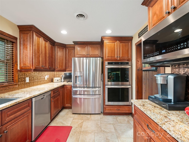 kitchen featuring brown cabinets, stainless steel appliances, visible vents, light stone countertops, and tasteful backsplash