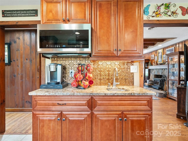 kitchen with light wood finished floors, a sink, stainless steel microwave, decorative backsplash, and a wood stove