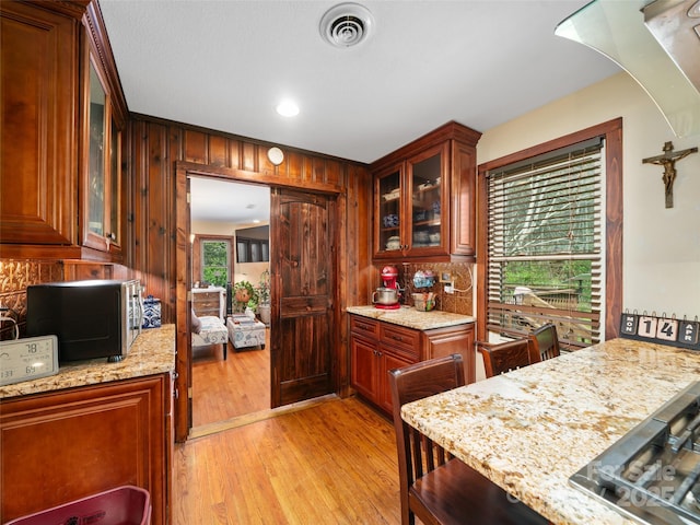 kitchen featuring light wood-style flooring, tasteful backsplash, visible vents, glass insert cabinets, and light stone counters