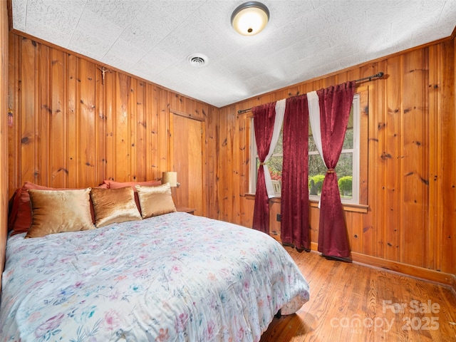 bedroom with wood finished floors, visible vents, and wood walls