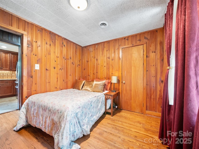 bedroom featuring wood walls, light wood finished floors, and visible vents