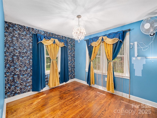 empty room featuring wood finished floors, a healthy amount of sunlight, baseboards, and an inviting chandelier