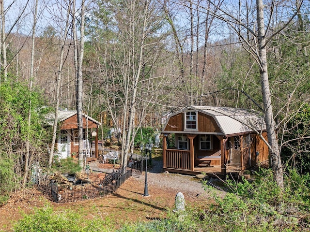 exterior space featuring a forest view, a gambrel roof, an outdoor structure, a porch, and metal roof