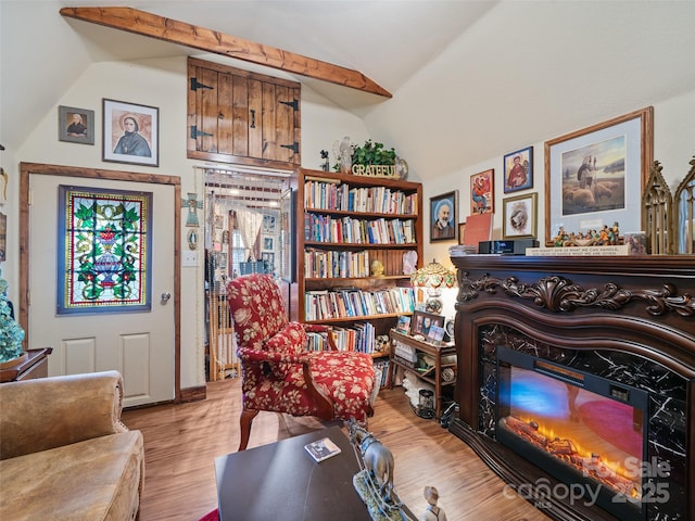 living area with light wood-style floors, vaulted ceiling, and a glass covered fireplace