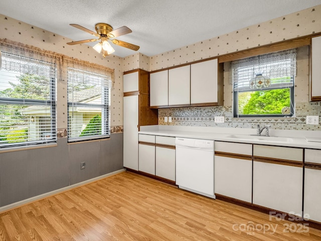 kitchen with light countertops, a sink, light wood-type flooring, wallpapered walls, and dishwasher