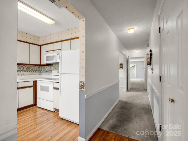 kitchen with a textured ceiling, decorative backsplash, white appliances, light countertops, and white cabinetry