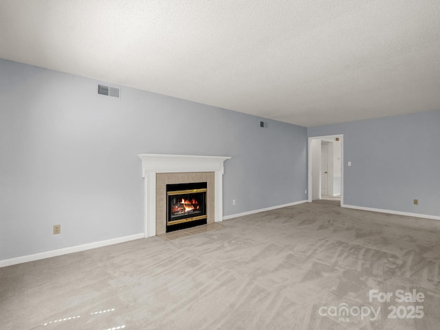 unfurnished living room with carpet, a textured ceiling, visible vents, and a tiled fireplace