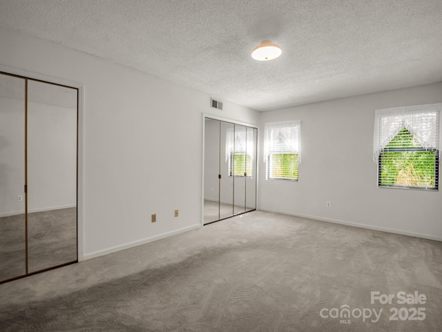 unfurnished bedroom featuring carpet flooring, a textured ceiling, baseboards, visible vents, and two closets