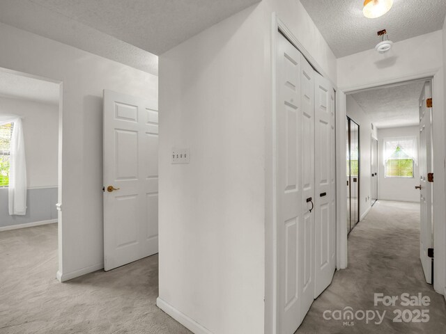 hall featuring light colored carpet, baseboards, and a textured ceiling