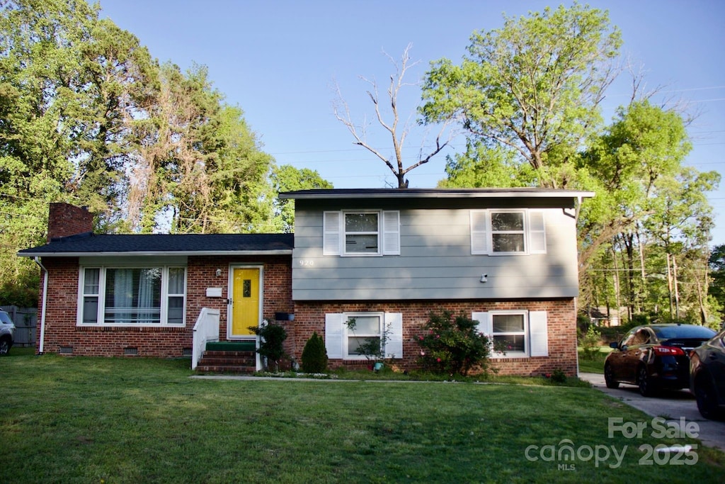 split level home with a chimney, brick siding, and a front yard