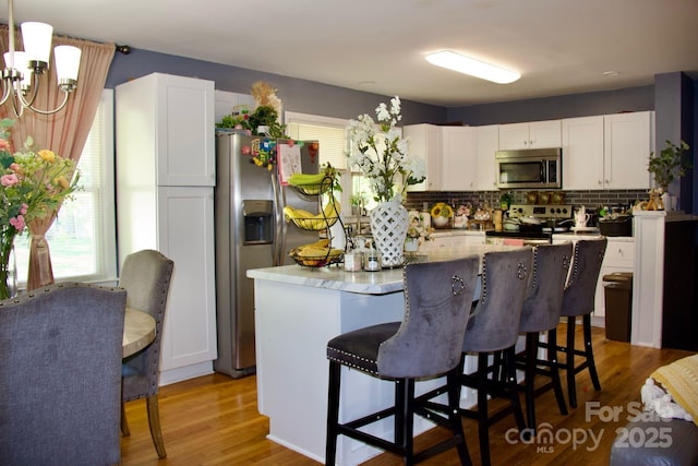 920 Squirrel Hill Rd, Charlotte, NC 28213 - kitchen featuring appliances with stainless steel finishes, white cabinets, wood finished floors, a center island, and a breakfast bar
