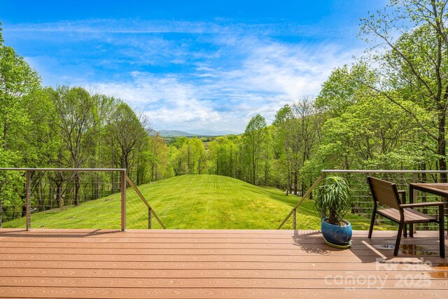 wooden deck with a lawn and a forest view