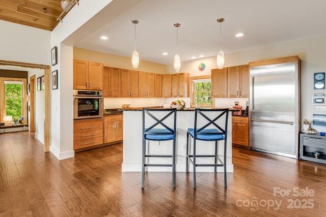 kitchen featuring dark countertops, stainless steel appliances, a kitchen bar, dark wood-style floors, and recessed lighting