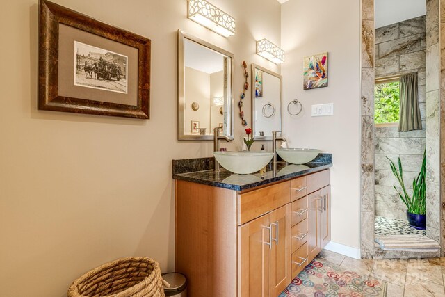 full bath featuring baseboards, a sink, double vanity, and tiled shower