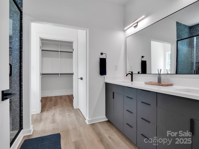 full bathroom with a sink, double vanity, wood finished floors, a spacious closet, and a stall shower
